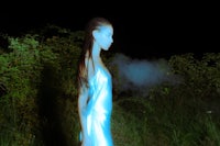 a woman in a blue dress standing in a field at night